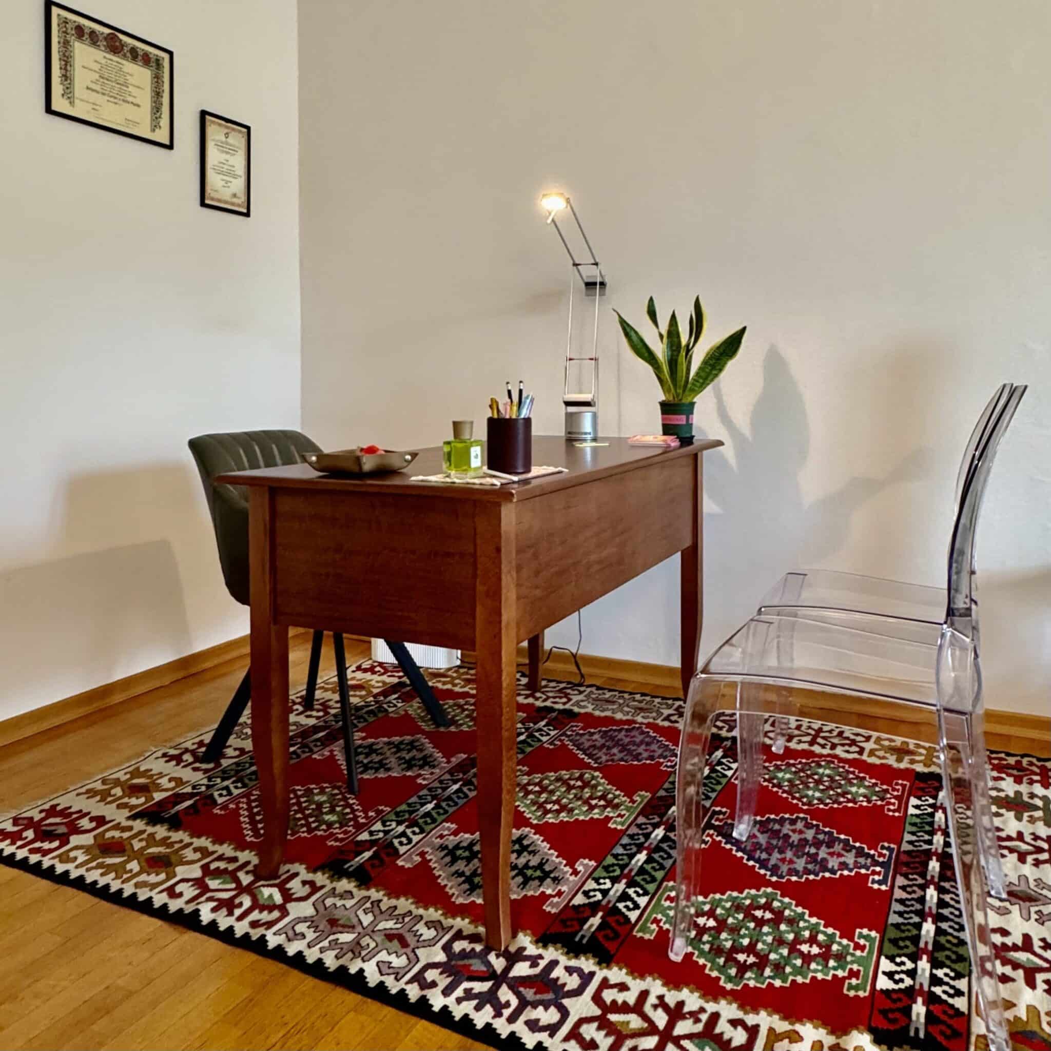 Scrivania dello studio psicologo Adriano Cacciola a Torino con sedia, tappeto orientale e certificati appesi al muro.